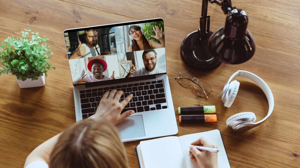 Remote work picture with laptop with video calling and a woman writing down notes while looking at coworkers